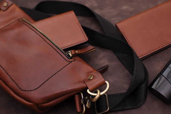 Produits en cuir marron: un sac à ceinture avec une sangle et un couvercle de passeport sur fond noir