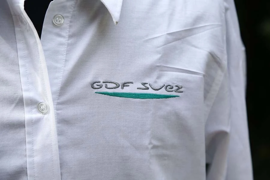 Professionnel en chemise blanche boutonnée portant un logo brodé "GDF SUEZ" avec soulignement vert sur la poche poitrine