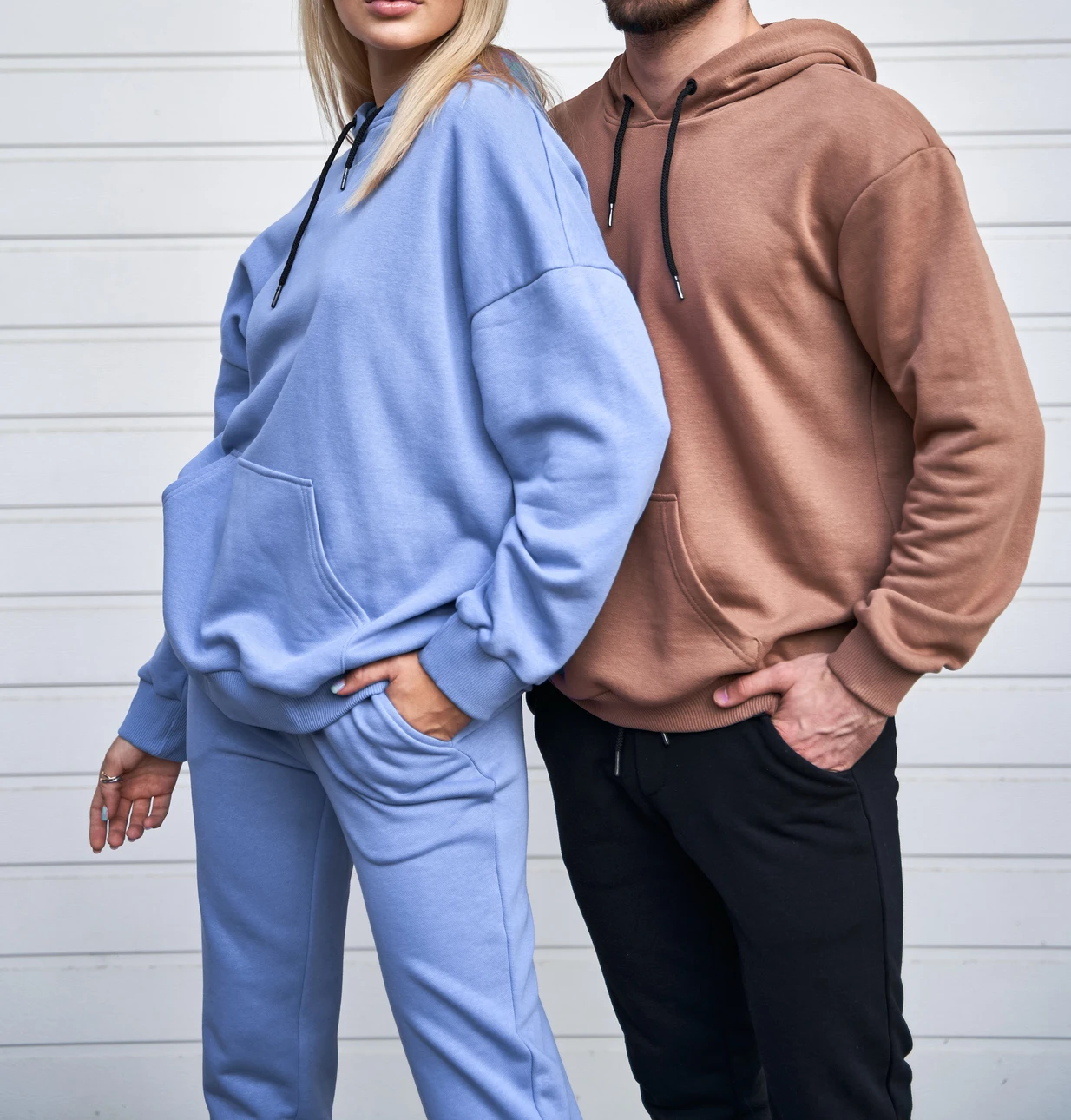 Homme souriant en sweat à capuche bleu faisant un pouce levé sur fond bleu uni, expression positive et confiante, geste d'approbation